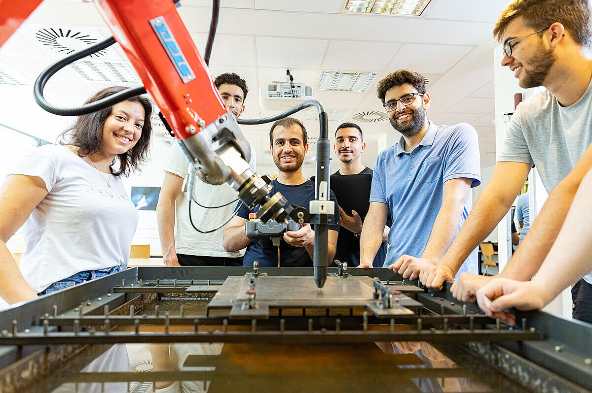 Portalöffnung Wintersemester 2025/26 Junge Menschen stehen an einem roten Industrieroboter und schauen in die Kamera.