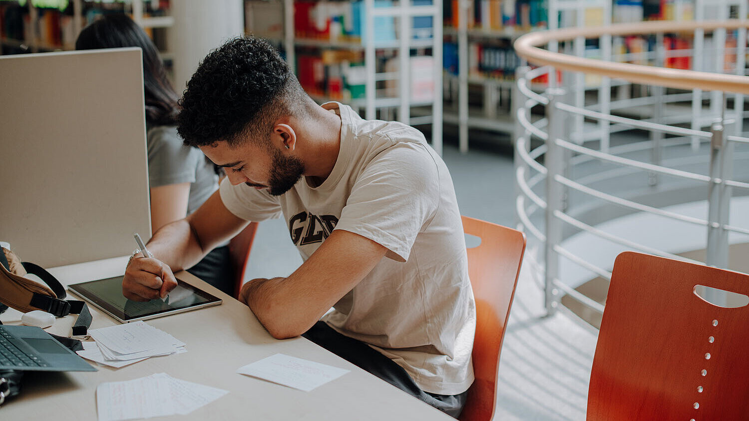 Arbeiten in der Bibliothek Ein Studierender sitzt an einem Einzelarbeitsplatz in der Bibliothek und schreibt etwas in sein Tablett