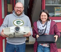 Ein Mitarbeiter und eine Mitarbeiter der Lebenshilfe Wetterau halten einen Beamer und mehrere Notebooks in den Händen.