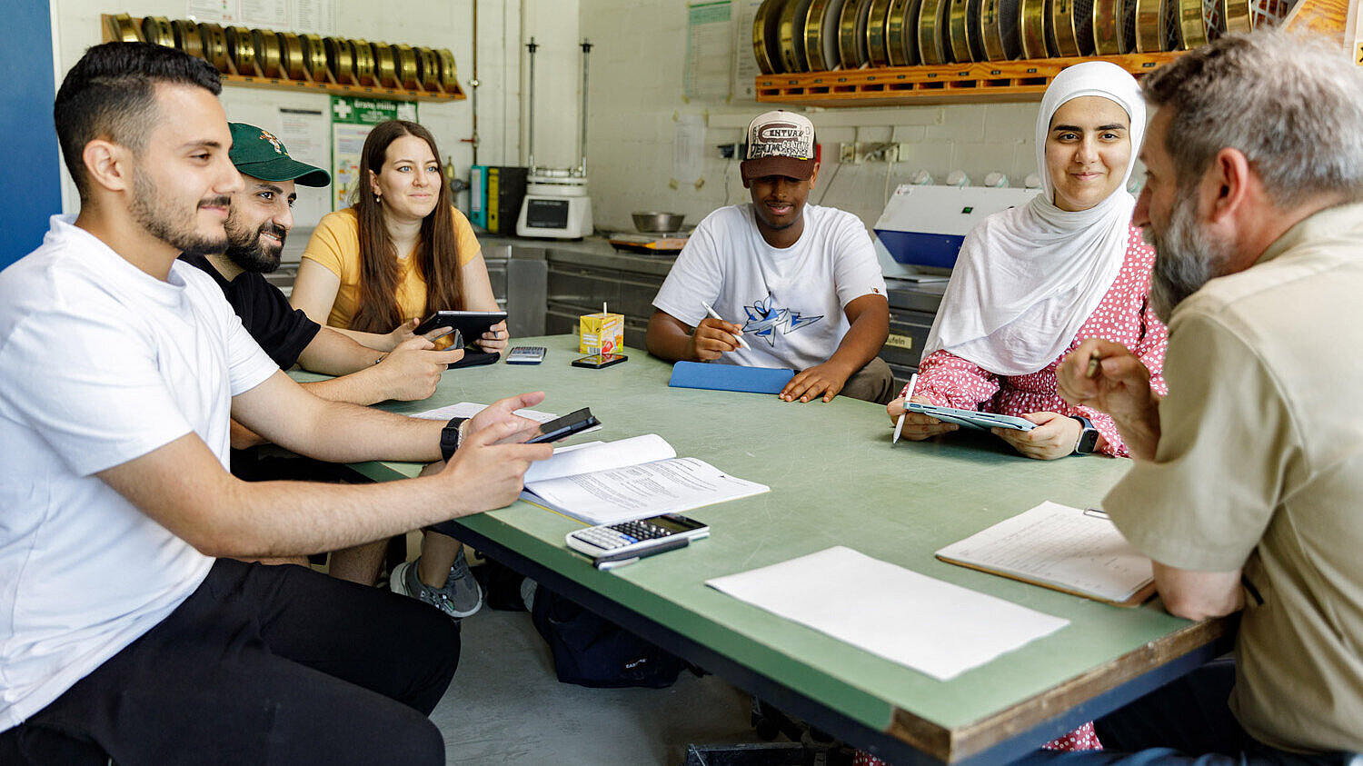 Arbeit in Kleingruppen Studierende und Dozent sitzen gemeinsam am Tisch und beraten sich