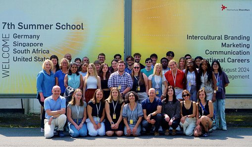 Gruppenfoto mit allen Beteiligten vor einer Werbeplakatwand für die Summer School.