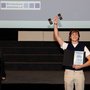 HSRM-Student Moritz Pähler steht während der Preisverleihung des exground filmfest 2024 auf der Bühne und reckt seinen Preis in die Höhe.