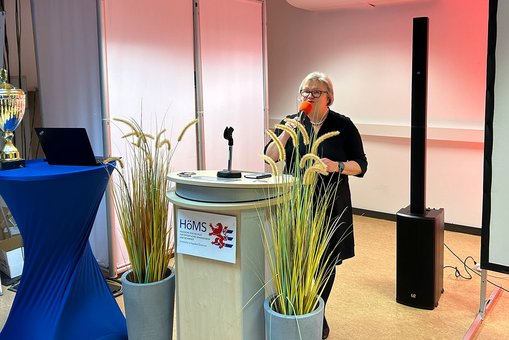 Prof. Dr. Eva Waller, Präsidentin der Hochschule RheinMain, steht mit einem Mikrofon in der Hand an einem Rednerpult und spricht zu den Gästen der Veranstaltung.