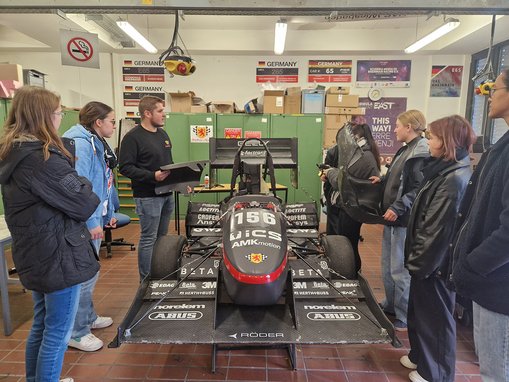 Die Teilnehmerinnen stehen in der Werkstatt des Formula Student Teams und betrachten das Rennauto Sandy