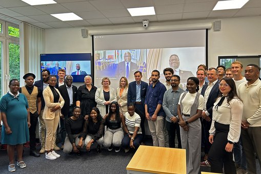 Gruppenfoto der Teilnehmenden des Hydrogen Safety Symposiums vor einer Leinwand, auf der digital zugeschaltete Teilnehmer zu sehen sind.