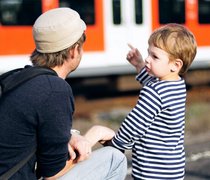 Vater mit seinem Sohn an einem Bahnsteig mit einem Zug im Hintergrund