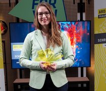 Maike Kaiser hält die Siegerinnen-Trophäe des ARD/ZDF Förderpreises „Frauen + Medientechnologie“ in den Händen.