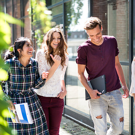 Studierende auf dem Campus Vier Studierende laufen auf dem Campus in der Sonne und lachen
