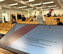 Blick über den Präsentationsbildschirm in einen Hörsaal der Hochschule RheinMain kurz vor Beginn des 10. Wiesbadener Versicherungskongresses