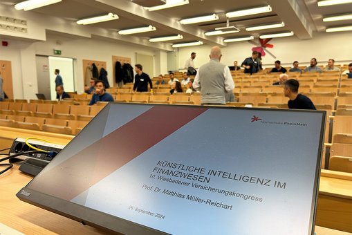 Blick über den Präsentationsbildschirm in einen Hörsaal der Hochschule RheinMain kurz vor Beginn des 10. Wiesbadener Versicherungskongresses