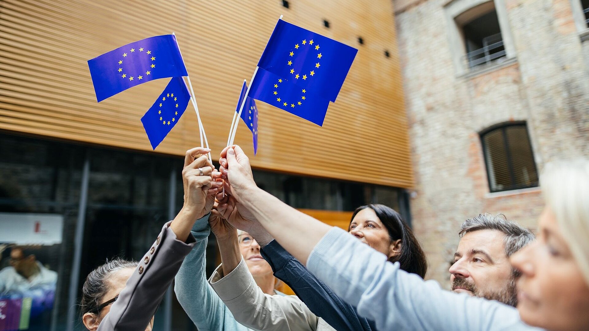 Europa hält zusammen Vier EU-Papierflaggen werden von vier Händen gemeinsam in die Höhe gehalten