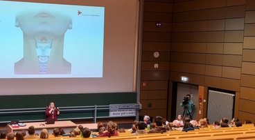 Heather Watson vom LehrLernZentrum demonstriert, dass der Kehlkopf vibriert, wenn man Geräusche erzeugt oder spricht. © Michaela Kreuzpointner | Hochschule RheinMain