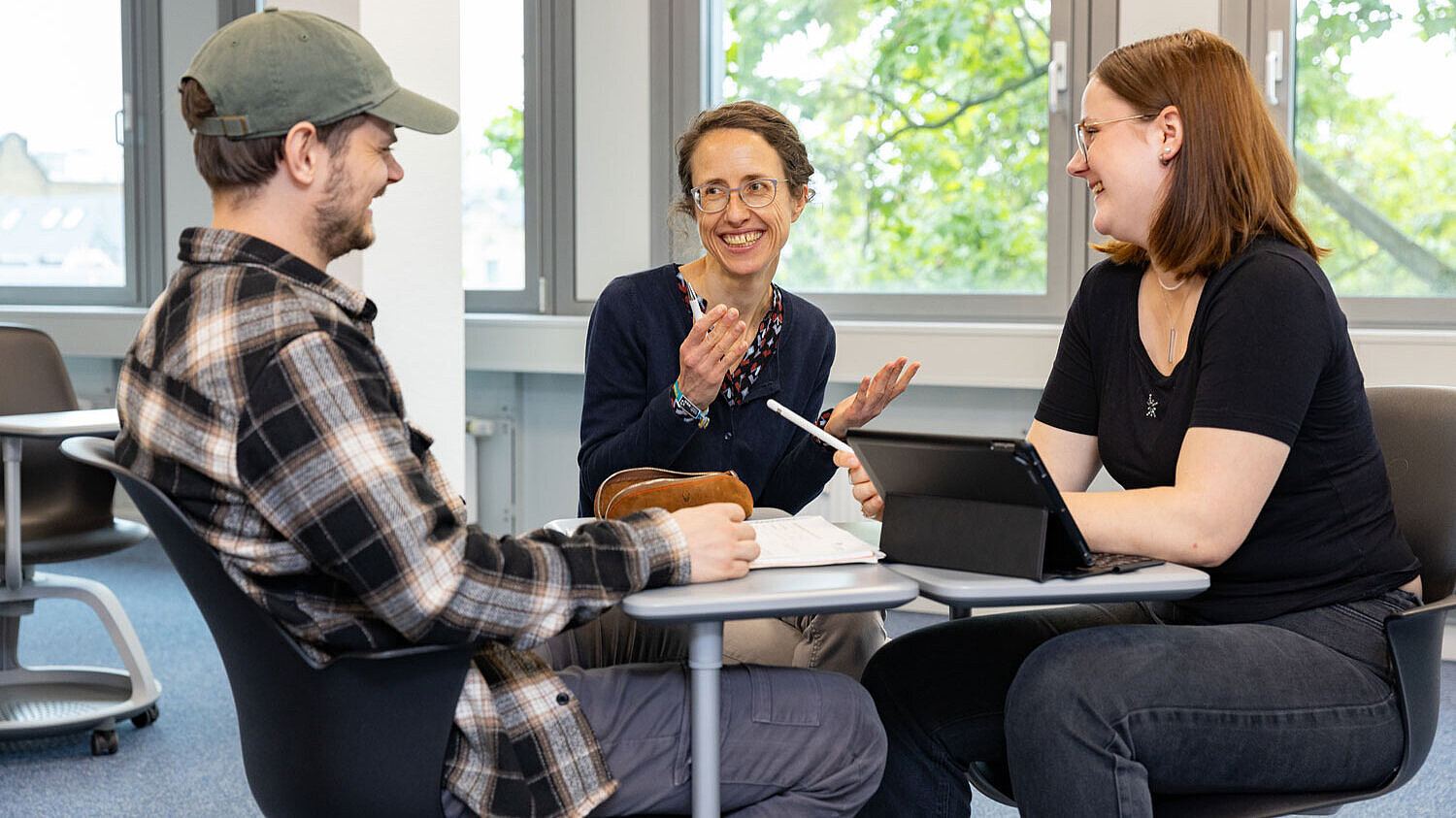 Beratungssituation Zwei Studierende sitzen sich an zwei schmalen Tischen gegenüber und simulieren ein Bewerbungsgespräch, zwischen Ihnen gibt eine Beraterin Tipps