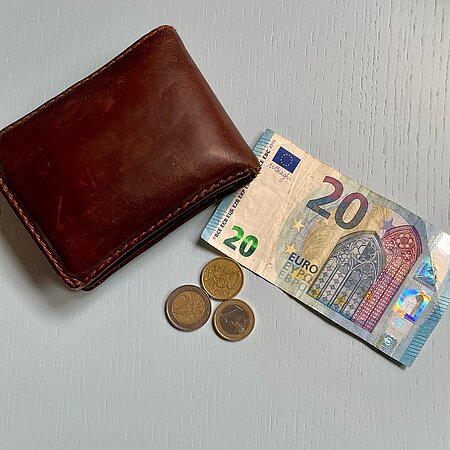 Geld Auf einem Tisch liegen Euro-Scheine, Euro-Münzen und ein brauner Geldbeutel aus Leder.