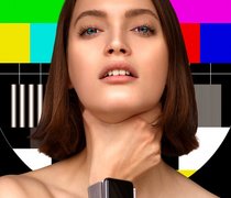 Junge Frau vor einem TV-Testbild und mit einer Smartwatch am Handgelenk fasst sich an den Hals und würgt sich selbst