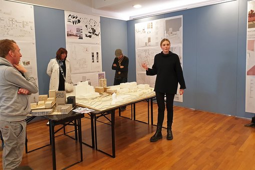 Die Bachelor-Absolventin Sophia Olivia Wolf steht vor ihrem Entwurf und erläutert Besucher:innen der Ausstellung ihre Arbeit